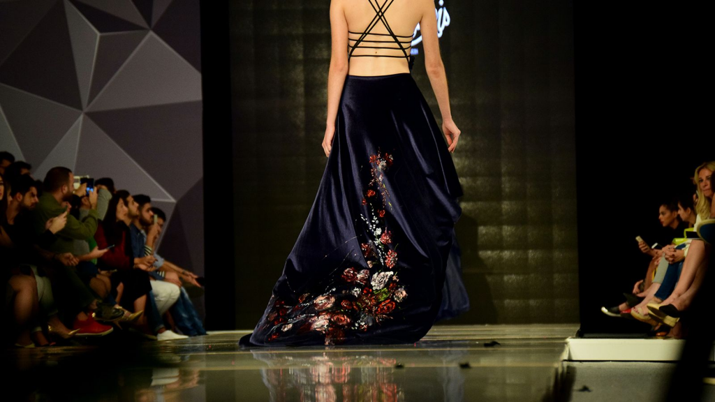 a model walking down a catwalk with her back turned to the camera, wearing a black dress with floral pattern